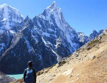 a solo woman traveller standing in front of a tall mountain in everest region while travelling alone with a guide from frolic adventure and the blue sky on a clear day.