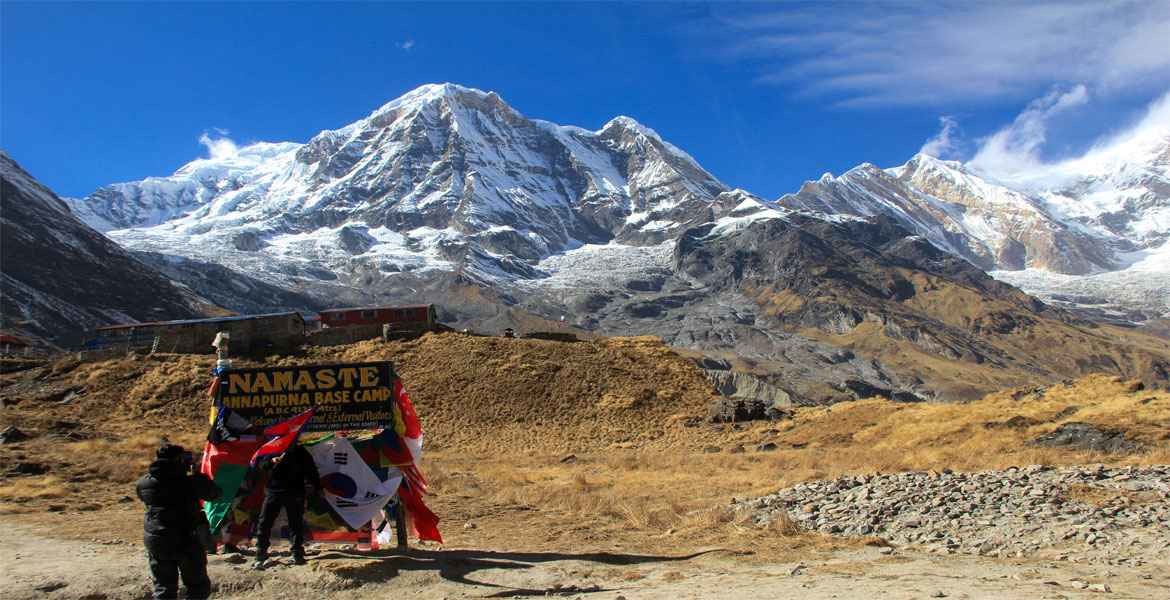 bright view of annapurna mountains with the blue sky and the trekkers are taking photo with information sign board at annapurna base camp.